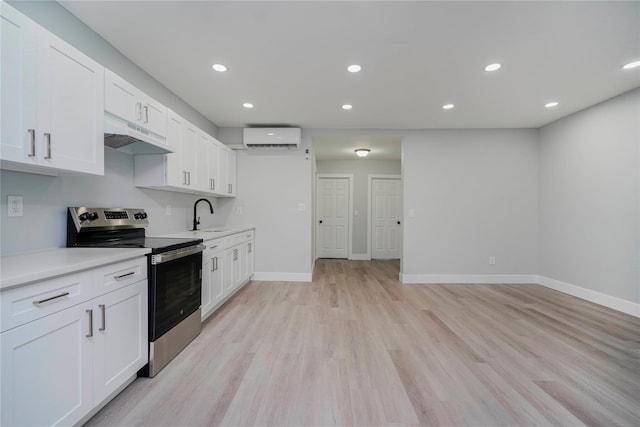 kitchen featuring stainless steel electric stove, a sink, an AC wall unit, light countertops, and under cabinet range hood