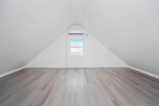 additional living space featuring light wood-style flooring, baseboards, a wall mounted AC, and lofted ceiling