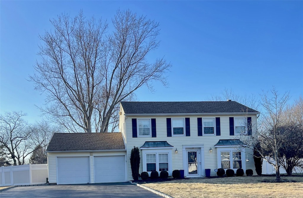 colonial-style house with a garage, roof with shingles, fence, and aphalt driveway