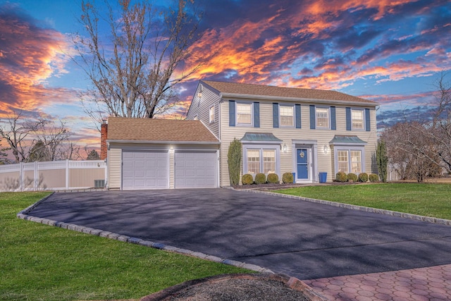 colonial inspired home featuring an attached garage, driveway, a front yard, and fence