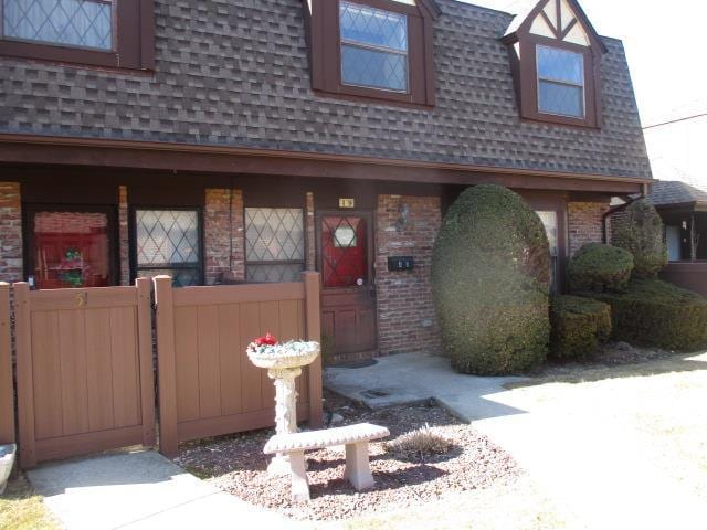 view of front of home featuring a shingled roof, mansard roof, and brick siding