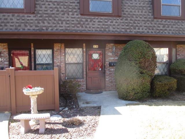 doorway to property featuring roof with shingles, brick siding, and mansard roof