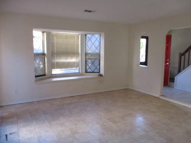 unfurnished room with plenty of natural light, stairway, and baseboards