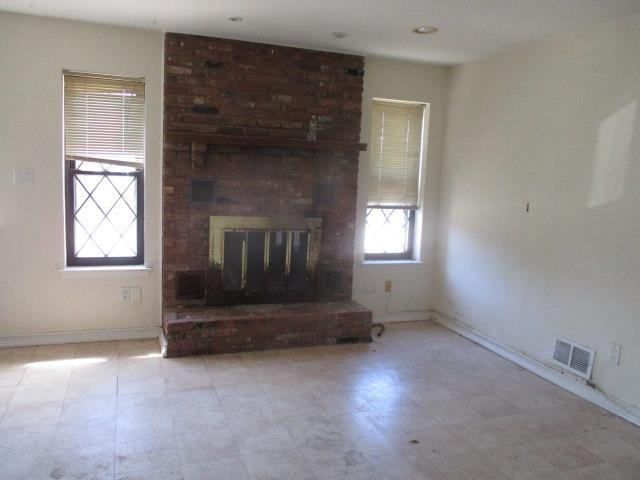 unfurnished living room with a brick fireplace, baseboards, and visible vents