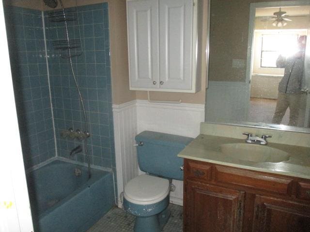 full bathroom featuring a ceiling fan, toilet, a wainscoted wall, shower / bathtub combination, and vanity