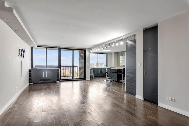 unfurnished living room with floor to ceiling windows, wood finished floors, bar area, and baseboards