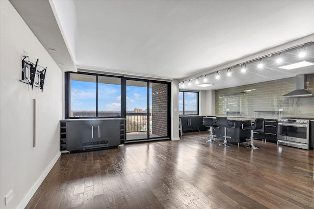 living room featuring a wall of windows, dark wood finished floors, bar area, and baseboards