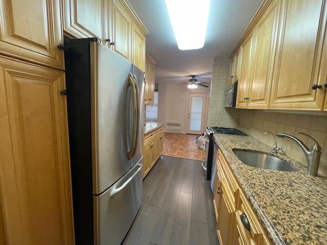 kitchen featuring dark wood-style floors, stainless steel appliances, decorative backsplash, a sink, and light stone countertops