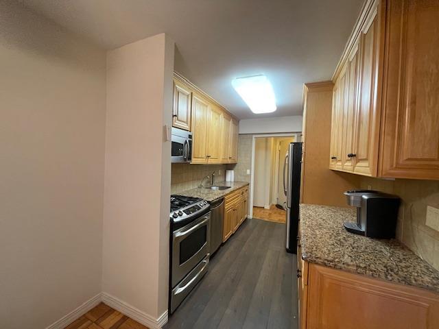 kitchen featuring stainless steel appliances, tasteful backsplash, a sink, light stone countertops, and baseboards