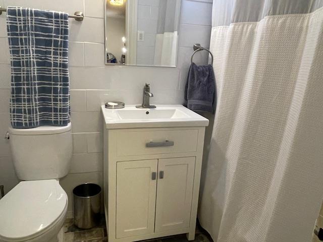 bathroom featuring toilet, tile walls, and vanity