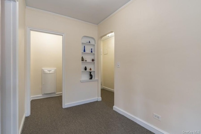 hallway featuring dark colored carpet, baseboards, built in shelves, and ornamental molding