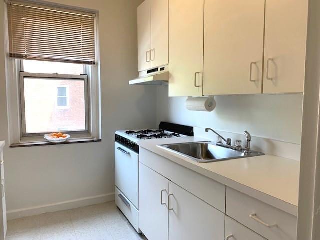 kitchen with baseboards, under cabinet range hood, light countertops, white gas range oven, and a sink