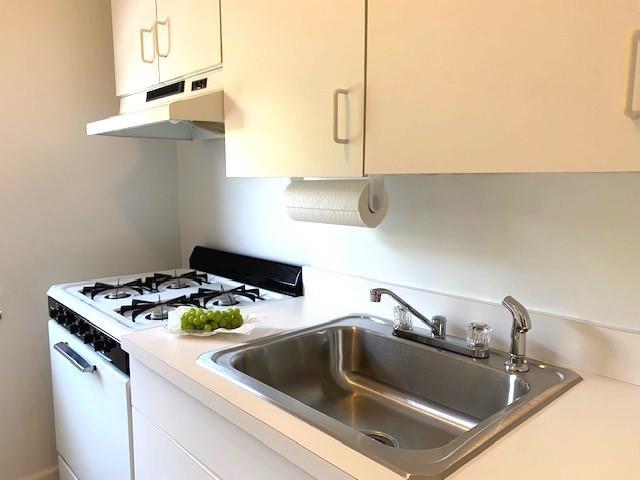 kitchen with under cabinet range hood, a sink, white cabinetry, light countertops, and white gas range