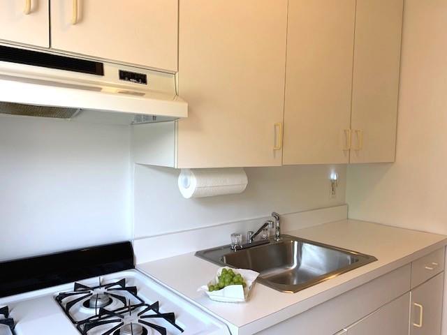 kitchen featuring under cabinet range hood, range, light countertops, and a sink