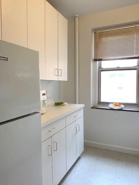 kitchen with white cabinetry, freestanding refrigerator, light countertops, light tile patterned floors, and baseboards