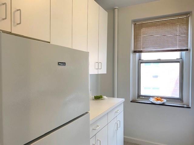 kitchen with baseboards, white cabinetry, light countertops, and freestanding refrigerator