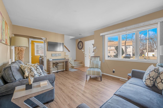 living area featuring light wood-style floors, baseboards, and stairway