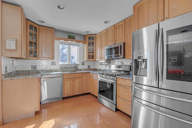 kitchen with tasteful backsplash, glass insert cabinets, light stone counters, stainless steel appliances, and a sink