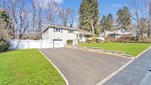 tri-level home featuring a garage, fence, aphalt driveway, and a front yard