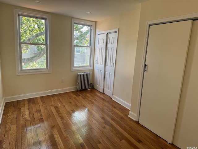 unfurnished bedroom featuring radiator, baseboards, and hardwood / wood-style flooring