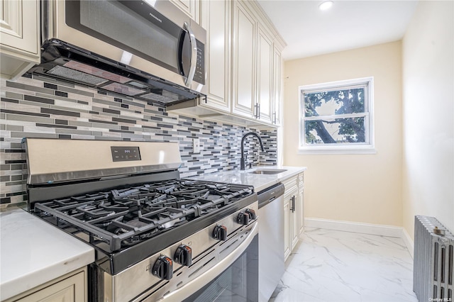 kitchen with baseboards, radiator heating unit, appliances with stainless steel finishes, marble finish floor, and a sink