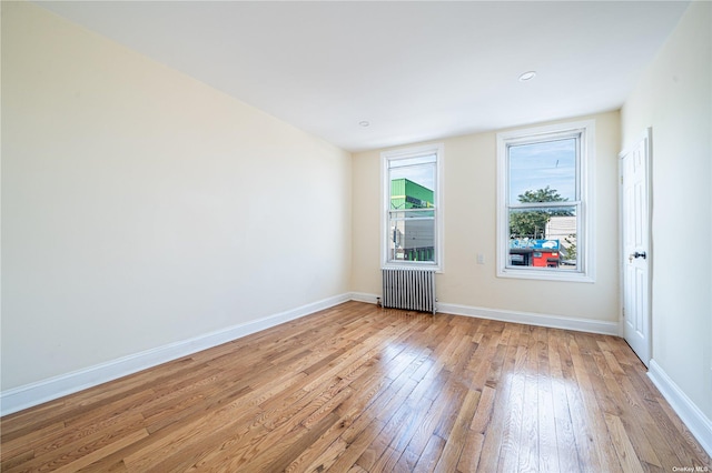 unfurnished room with baseboards, radiator heating unit, and light wood-style floors