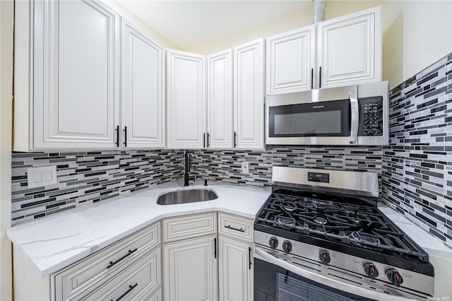 kitchen featuring decorative backsplash, appliances with stainless steel finishes, white cabinets, and a sink