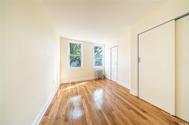 unfurnished room featuring radiator, light wood-type flooring, and baseboards