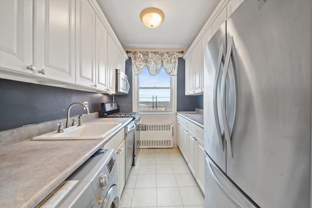 kitchen with radiator heating unit, appliances with stainless steel finishes, white cabinetry, a sink, and washer / dryer