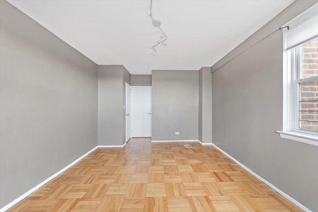 spare room featuring rail lighting and baseboards