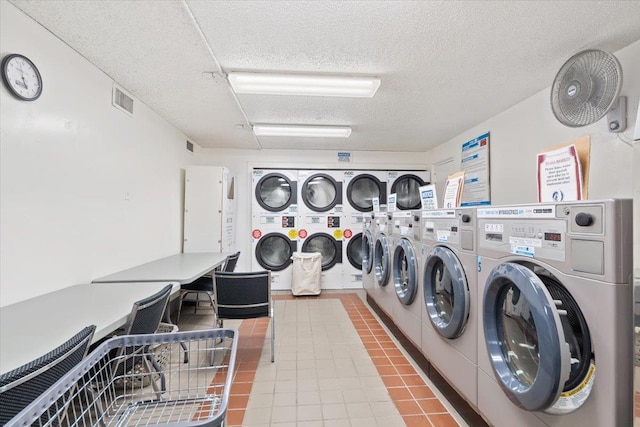 community laundry room with a textured ceiling, visible vents, stacked washing maching and dryer, tile patterned floors, and washing machine and clothes dryer