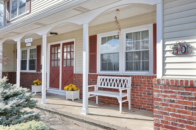 doorway to property featuring covered porch and brick siding