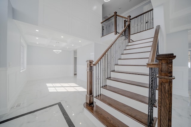 stairway featuring recessed lighting, a wainscoted wall, a decorative wall, a towering ceiling, and marble finish floor