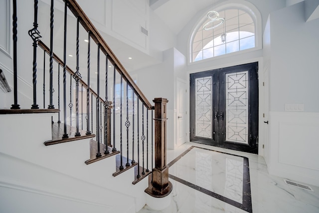 foyer entrance with a decorative wall, visible vents, marble finish floor, french doors, and wainscoting