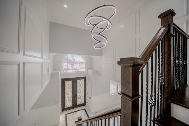entryway featuring stairway, crown molding, french doors, a chandelier, and a decorative wall