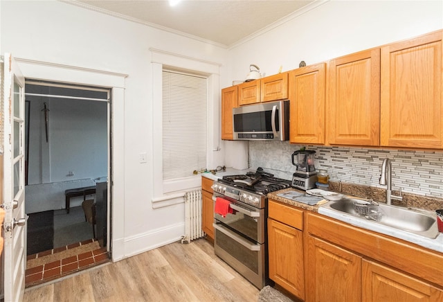 kitchen featuring radiator heating unit, appliances with stainless steel finishes, a sink, light wood-type flooring, and backsplash