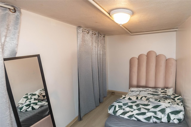 bedroom with light wood-style floors, baseboards, and a textured ceiling