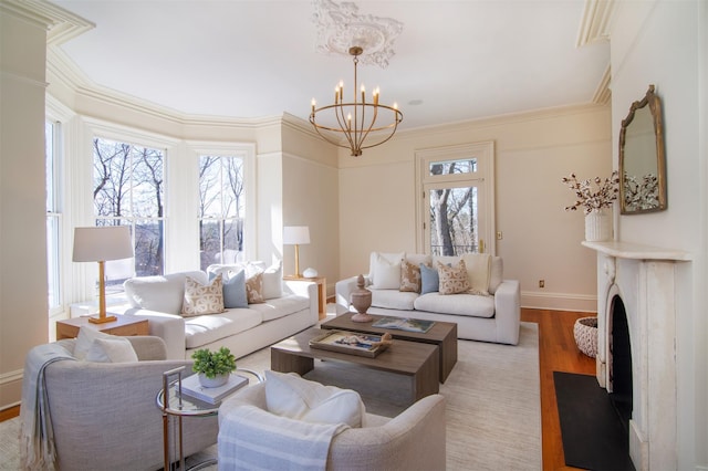 living room with a fireplace, ornamental molding, a chandelier, light wood-type flooring, and baseboards