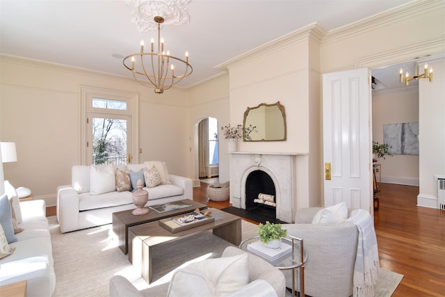 living area with a high end fireplace, arched walkways, a notable chandelier, and wood finished floors