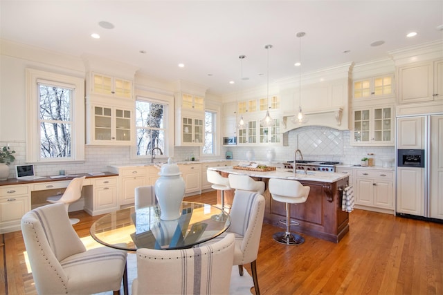 kitchen with crown molding, a center island with sink, light wood-style floors, paneled built in refrigerator, and a kitchen breakfast bar