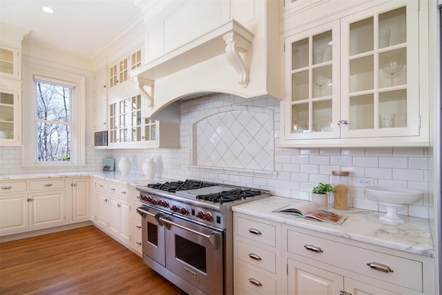 kitchen with range with two ovens, premium range hood, ornamental molding, light wood finished floors, and tasteful backsplash