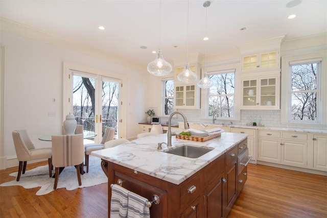 kitchen with plenty of natural light, an island with sink, glass insert cabinets, light wood-style floors, and a sink