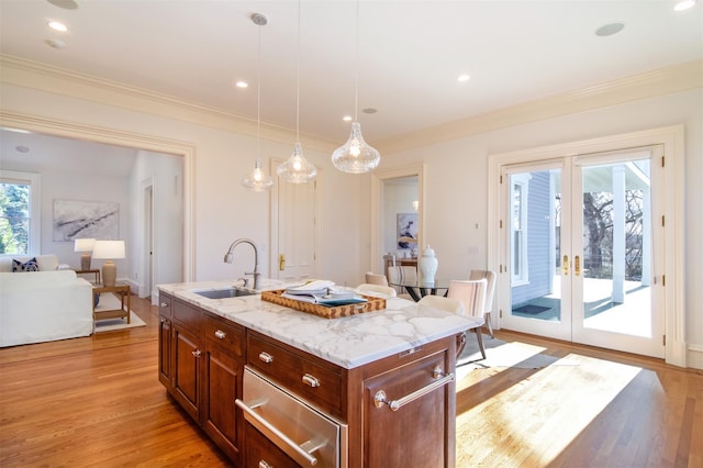 kitchen featuring light wood-style flooring, ornamental molding, a sink, and decorative light fixtures