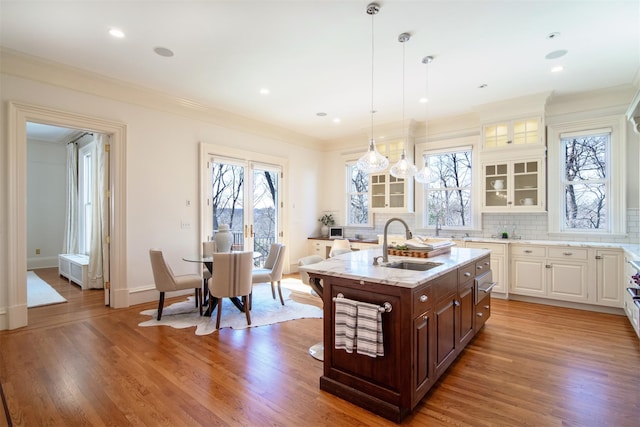 kitchen with crown molding, glass insert cabinets, a sink, and light wood finished floors