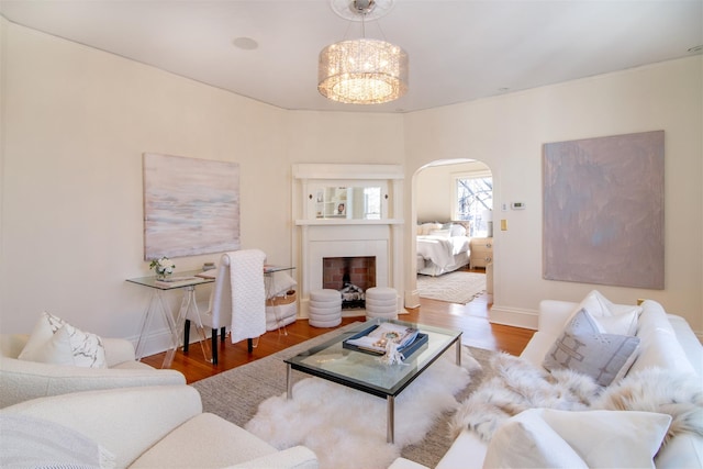 living room with arched walkways, a notable chandelier, a fireplace, wood finished floors, and baseboards