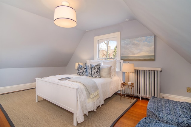 bedroom featuring radiator heating unit, baseboards, vaulted ceiling, and wood finished floors