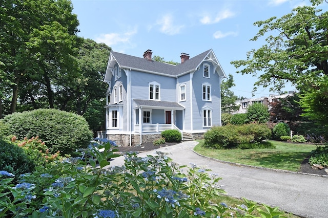 victorian-style house featuring covered porch, a shingled roof, a chimney, and aphalt driveway