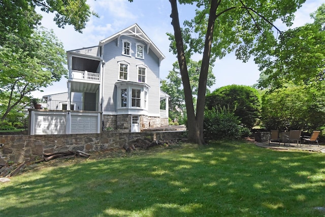 rear view of property with a patio, a lawn, stone siding, and a balcony