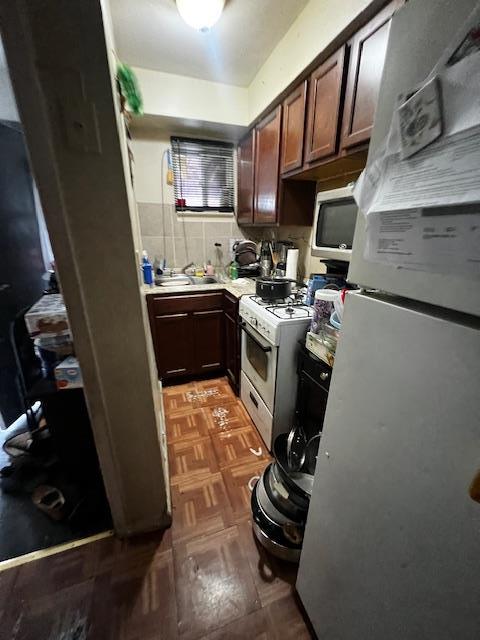 kitchen with white appliances, a sink, light countertops, dark brown cabinets, and backsplash