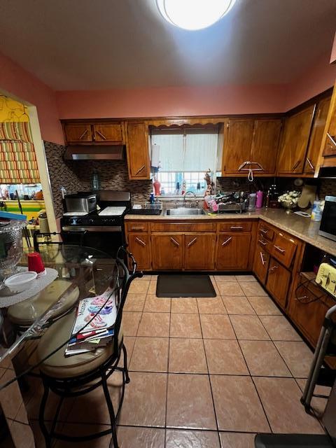 kitchen featuring gas range oven, tasteful backsplash, light tile patterned floors, a sink, and under cabinet range hood